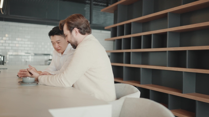 Positive multinational colleagues talking about work and looking at phone in the office