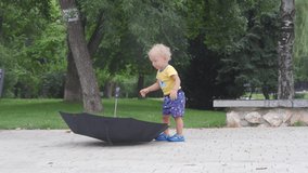 Little child walking in the park on a rainy summer day, 1.5 year old toddler kid playing with black umbrella for rain.