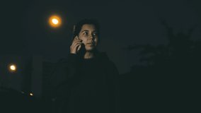 Young female standing outside in darkness and talking on phone in front of flashlights. Busy young woman student having a call at night or in the evening