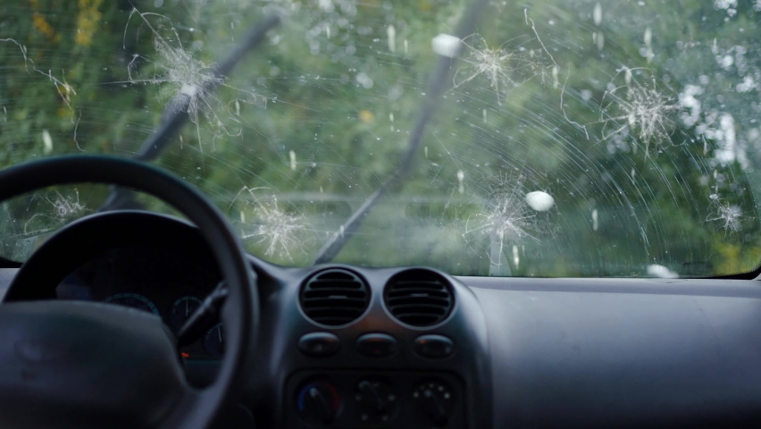 A broken car windshield and falling hail during a natural disaster storm