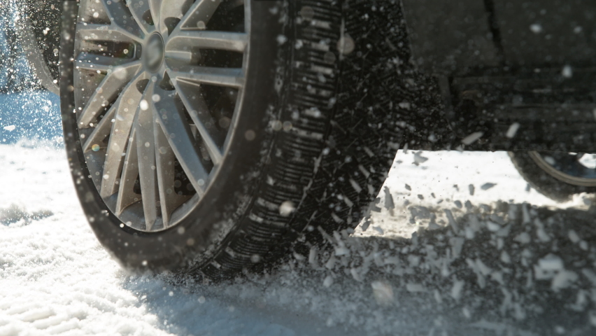 SLOW MOTION TIME WARP, LOW ANGLE, CLOSE UP, DOF: Powerful vehicle struggling to gain traction on the winter road spews up pieces of snow. Wheels spin in place while trying to drive along snowy street. Royalty-Free Stock Footage #1094435679