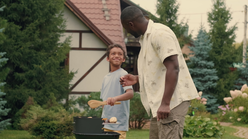 African dad and African son are cooking grilled vegetables near the house on the lawn.Multiracial Family,Mixed Race,Diverse People,Multiethnic Relations Royalty-Free Stock Footage #1094438131
