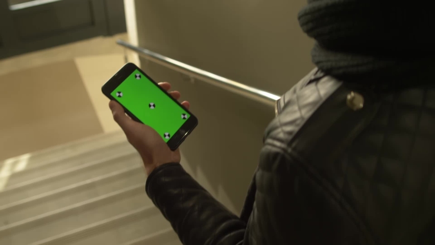 Man holding phone in one hand with green screen 
