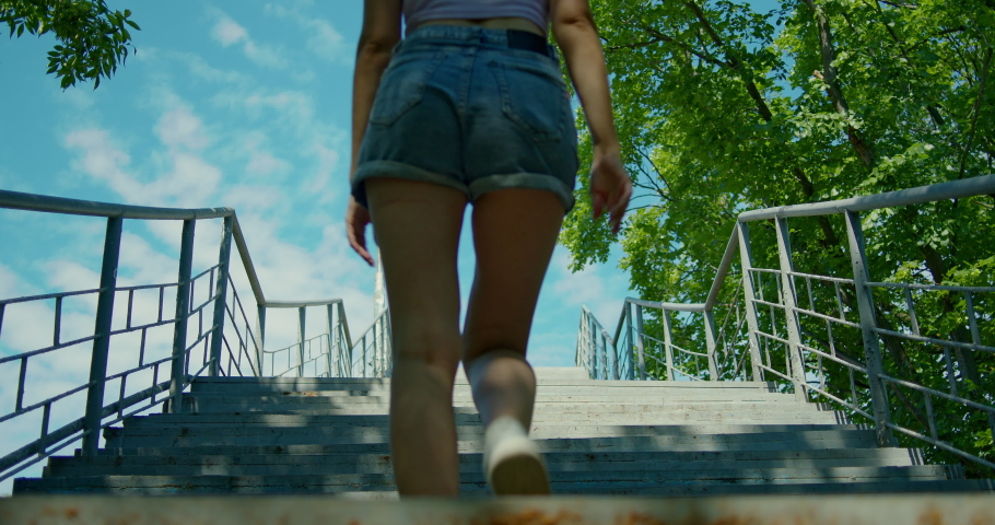 A young girl climbs a long concrete staircase up, in shorts, sneakers, sunglasses.