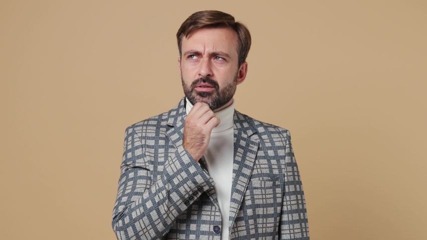 Young employee business man corporate lawyer 30s wear classic formal grey suit jacket look aside prop up chin iterates over solution options work in office isolated on plain pastel beige background | Shutterstock HD Video #1094455363