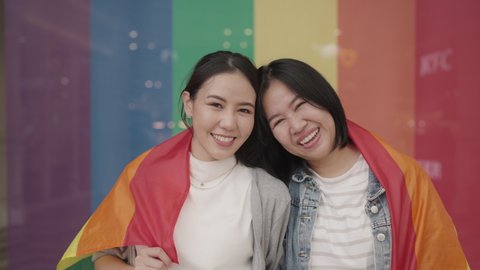 Portrait young adult queer lover transgender asia two gay people fun happy waving hold colorful flag. Proud of LGBT LGBTQIA culture color bisexual family festival hug love smile at city street town. วิดีโอสต็อก