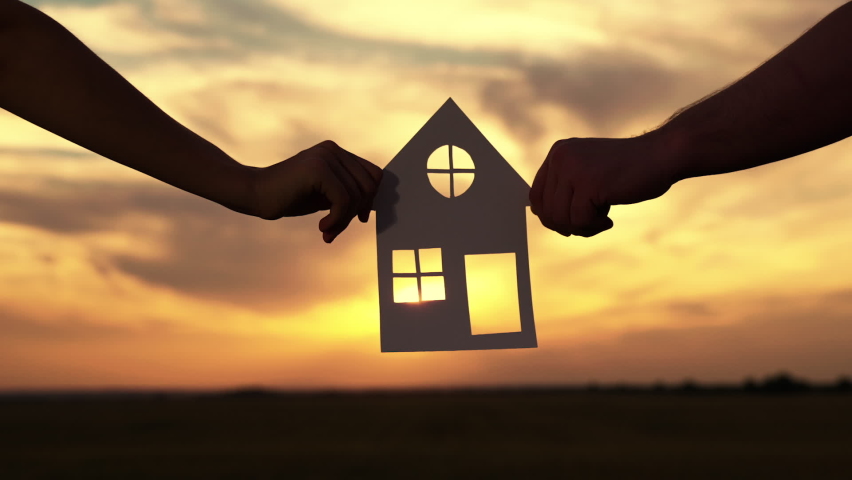 Symbol of house, happiness. Home for children and parents, Familys hands are holding paper house at sunset, sun is shining through window. Concept of building house for family. Dream to buy house. Royalty-Free Stock Footage #1094459389