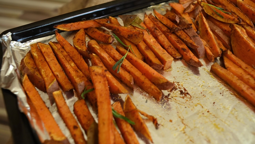 Healthy homemade sweet potato fries on a baking sheet. Delicious vegan meal - roasted batata wedges baked with rosemary leaves. Close-up. Delicious healthy vegan meal. | Shutterstock HD Video #1094460371