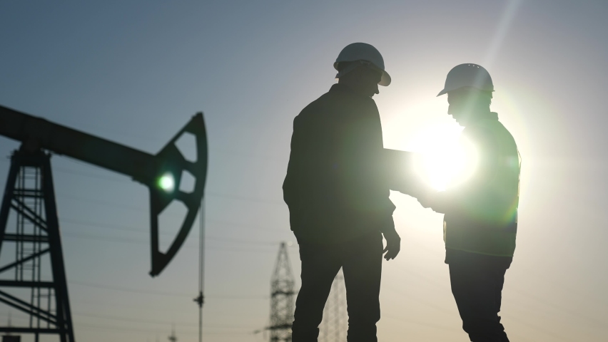oil production. two silhouette workers work as a team next to an oil pump. business oil production production concept. two engineers of the oil and gas industry are discussing a sun business plan Royalty-Free Stock Footage #1094463679