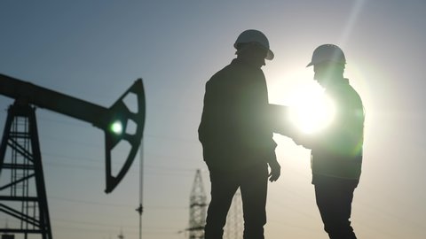 oil production. two silhouette workers work as a team next to an oil pump. business oil production production concept. two engineers of the oil and gas industry are discussing a sun business plan : vidéo de stock