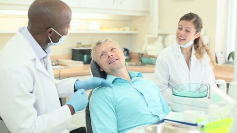 Dentist with patient and dental assistant talking to each other and smiling. The dentist pats the patient reassuringly on the shoulder.