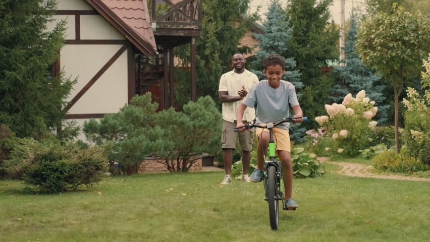 An African father teaches his son to ride a bike on his lawn.Multiracial Family,Mixed Race,Diverse People,Multiethnic Relations Royalty-Free Stock Footage #1094472649