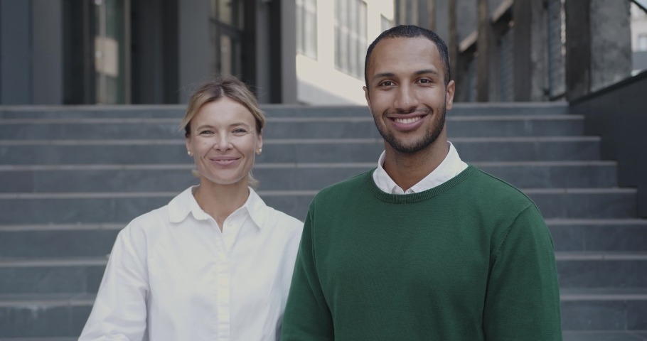 Portrait of Multiracial Young Man and Senior Woman Posing at Street. Elegant Colleagues Standing on Street Together. Corporate Building Background 