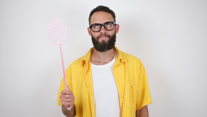Young caucasian charismatic man holding a fly swatter wanting to kill annoying mosquito or a fly.