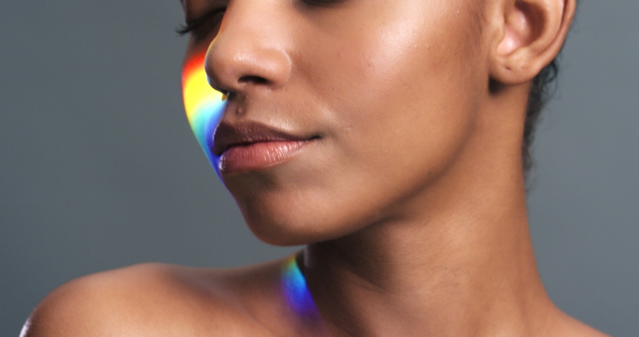 Model smile with rainbow light on face against grey studio background or wall. Black woman in beauty or skincare has iridescent neon lighting shine on skin in wellness or cosmetic portrait.