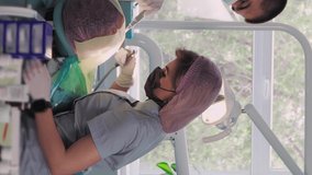 Vertical video, Two dentist doctors in medical masks, a man and a woman in a dental office, perform an operation on the teeth. Dentistry. Healthcare and Medicine Concept.