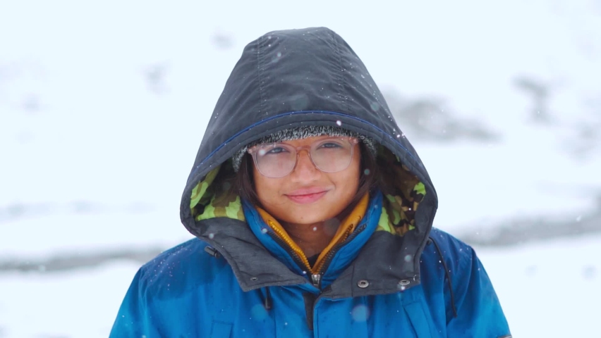 Close up portrait of happy Indian woman standing in snowfall and smiling at camera while hiking on mountain during winter at Manali in Himachal Pradesh, India. Winter holidays and adventure concept | Shutterstock HD Video #1094478279
