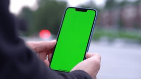 Man Using Smartphone in Vertical Mode with Green Mock-up Screen Outdoors, Doing Swiping, Scrolling Gestures. Internet Social Networks Browsing News, Financial Reports
