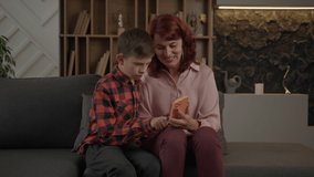 Mother learning her autistic son how to use mobile phone sitting on the couch at home. Boy with autism using smartphone with mom's help. - Powered by Shutterstock - Get 15% off with code: PIKWIZARD15