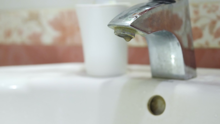 Woman's hand open the tap, rusty water running into a white sink. Hazardous tap water flows in sink. Terrible rusty water. Unfit for drinking water pipes. Sewer drain. Environmental pollution concept. Royalty-Free Stock Footage #1094482521