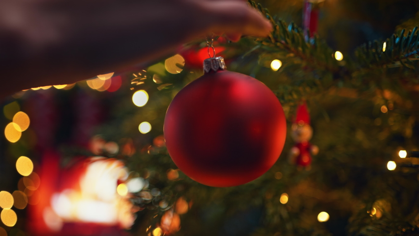 Decorating Christmas Tree with Red Glass Bauble in Slow Motion, Burning Fireplace in the Background | Shutterstock HD Video #1094486157