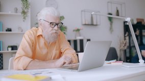 Trendy senior man resting from work, watching videos on laptop, procrastinating