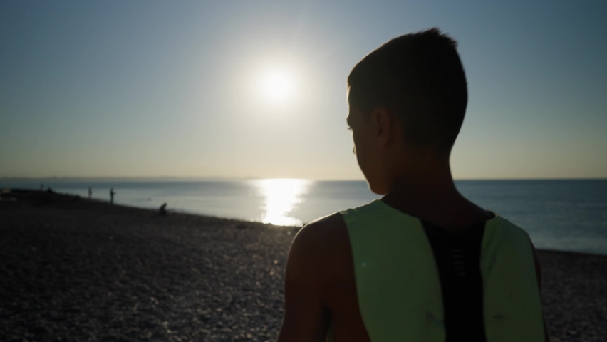 Young male boxer or karate fighter training on the beach during sunrise. Silhouette shot of boy doing shadow boxing in the morning. High quality 4k footage