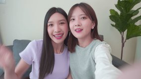 Teenager asian couple women feeling happy smile. While video call, selfie and look at camera mobile phone sitting sofa  in living room at home. Vacation lifestyle woman at home concept.