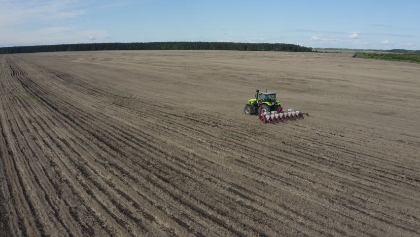 A tractor of bright colors drives through a field without vegetation and leaves pronounced stripes in its wake. Special equipment plows the ground for planting | Shutterstock HD Video #1094495323