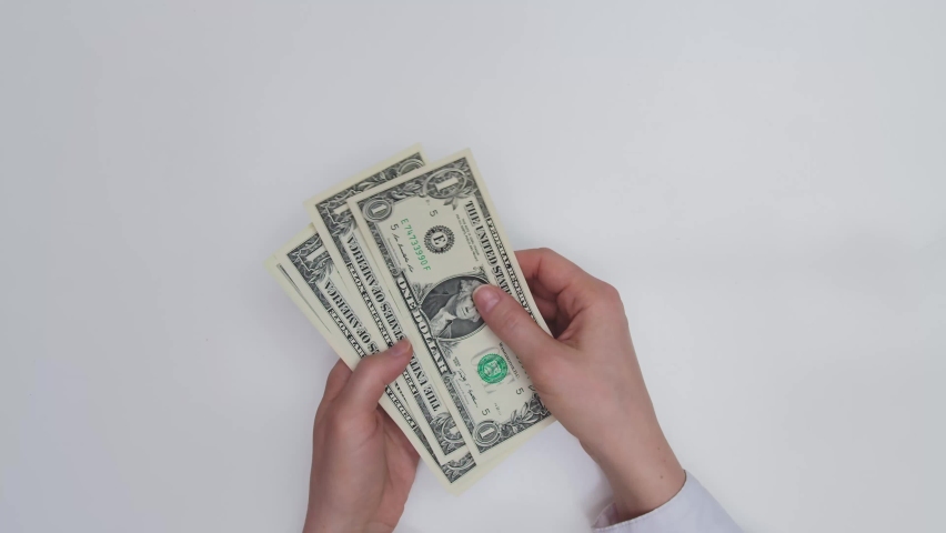 The hands of a man in a white shirt are counting a small bundle of dollars. He puts them on the table. Here you can see bills of one, two and twenty dollars | Shutterstock HD Video #1094495325