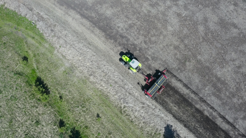Top view of a green tractor that plows the ground. Behind him remains a bright black strip of earth, which has been loosened. Left green stripe | Shutterstock HD Video #1094495333