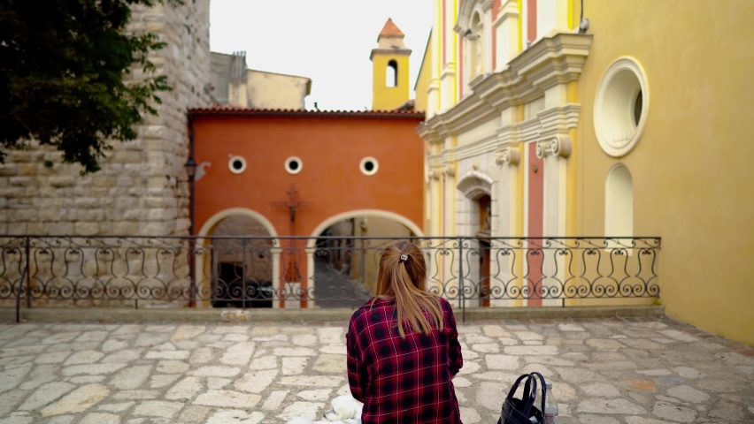 Notre Dame de la Platea in Antibes. The old quarter of Antibes. The girl is sitting on a stone bench near the church. Church landmark of the city of Antibes in France.