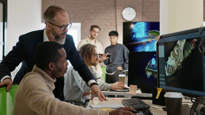 The CEO of the company studio developers of games and applications discusses with the artist a 3D model on a computer against the background of other employees of the company.