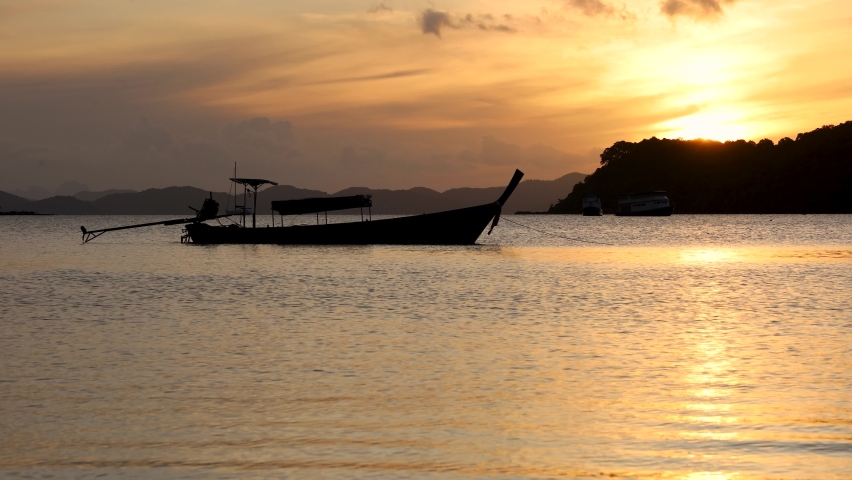 A silhouette of Phuket long tail boat floating in calm water at Ao Por pier while sunrise over Naka island in the background of Phang Nga Bay. Time-lapse video taken.  Royalty-Free Stock Footage #1094505239