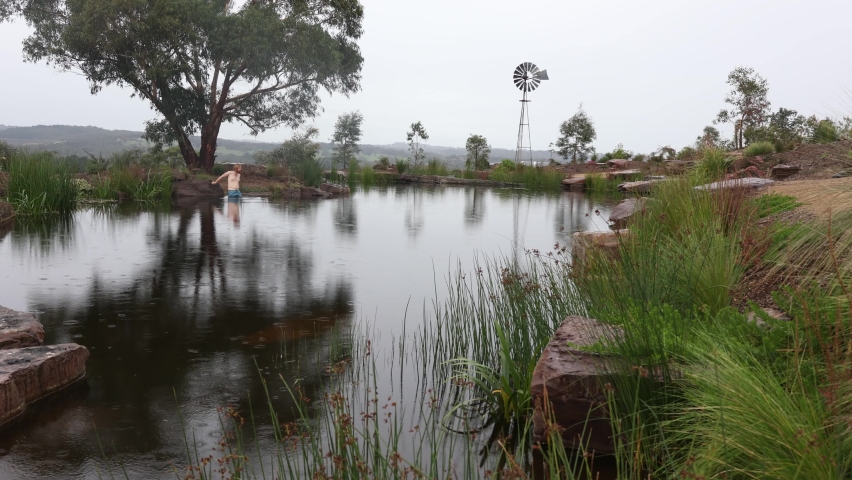 A man does cold water swimming in his farm dam while it is raining in Australia.