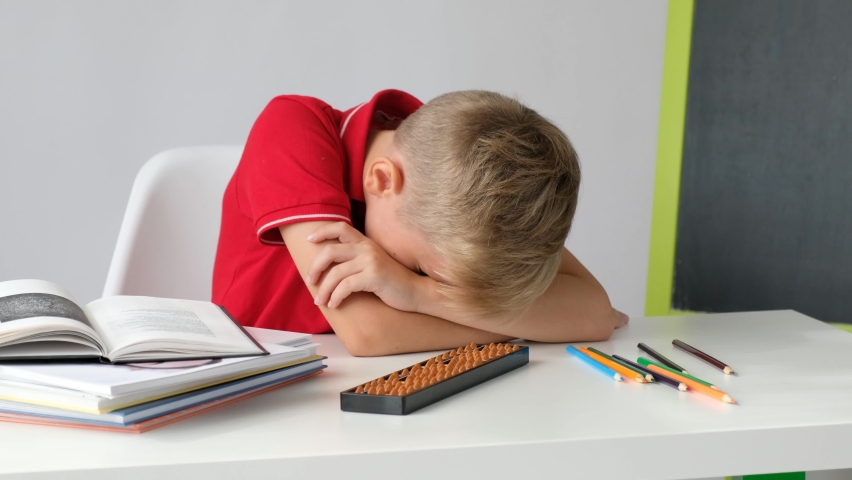 Cute school boy feeling tired bored and sleepy doing school homework at the table. | Shutterstock HD Video #1094510915