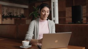 Smiling young brunette woman looking at camera in headset, conversation with business client online. Pleasant female job applicant answering of questions at video call interview meeting