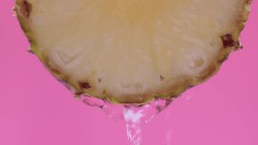Water drips flowing from a sliced sweet and fresh pineapple down on a pink background, fruit for frash and natural juice, cold diet drink with vitamin c. Slow motion, filmed on cinema camera, 4K.