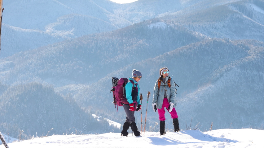 girl gives high five to a friend, two women climbed to the top of the mountain during a winter hike, winter hike, snowy mountains.