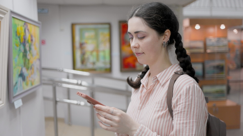 Culture and modern education. Portrait of smiling student using a smartphone. Virtual excursion with audio guide in the art gallery. Slow motion. Exhibition and visit to the museum. | Shutterstock HD Video #1094517197