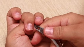 Person hand carefully cut cuticle on nails with clippers closeup, table background. Self care nails at home, manicure, manicured hands. Protective cover of nail plate. Beauty treatment concept.