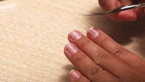 Person hand carefully clean dirt under nails by scissors closeup, table background. Delicate self care nails at home, manicure, manicured hands. Cleaning of nail plate. Beauty treatment concept.