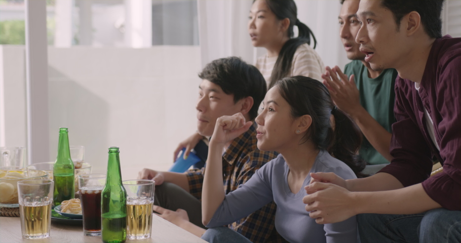 Group of young adult friend man and woman asia people sit at sofa couch joy chanting party fun game FIFA world cup live TV at home eat snack bowl drink beer bottle glass jump mad happy win exult face. Royalty-Free Stock Footage #1094525847