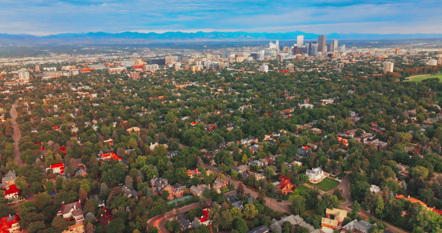 Densely built city scenery with lots of green trees. Panorama of Denver, Colorado with few skyscrapers standing out from usual architecture. Blue line of mountains in horizon at backdrop.