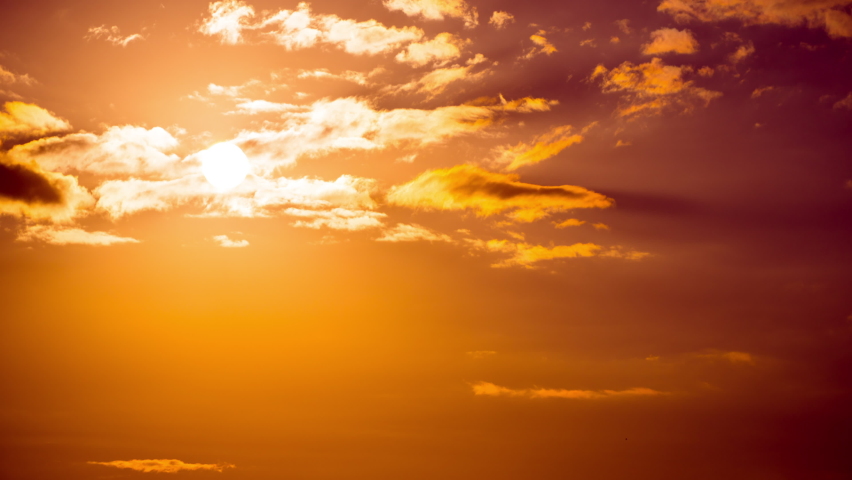 Time lapse bright orange sunset sun sets behind the clouds. The end of the day, the sun goes below the horizon. Big red hot sun in warm air distortion above the horizon.