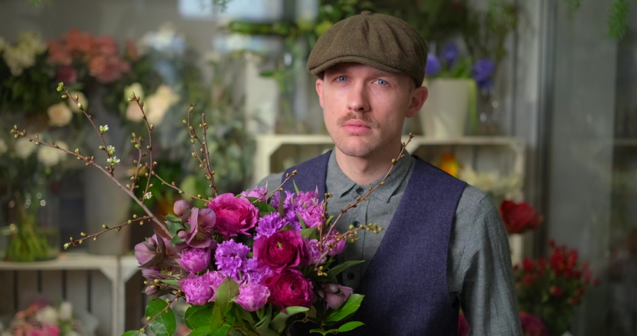 Women's Day or Valentine's Day concept. Attractive male in peaked cap and vintage clothes from 20s holding beautiful bouquet of red and violet flowers. Congratulating with flowers. 4k video footage Royalty-Free Stock Footage #1094529425