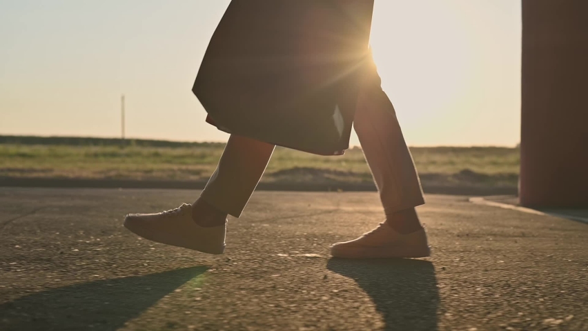 Young attractive girl in beige jeans and white sneakers walks through the street parking of shopping center with purchases in paper bags at sunset close-up. Cinematic footage, slow motion