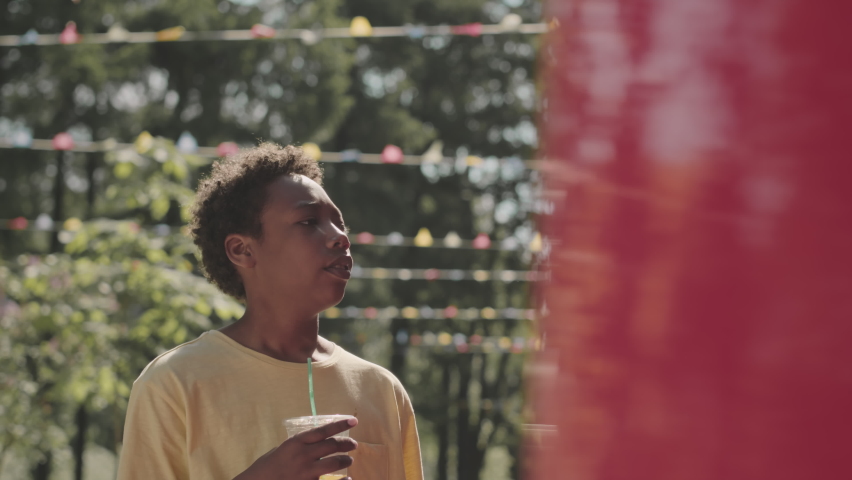 Waist up shot of Black man with his teenage son spending time together walking in park on hot sunny day