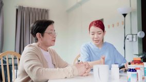 Asian woman nurse holding a medicine bottle and telling information to Asian senior woman before administering medication. Caregiver visit at home. Home health care concept. 4k slow motion video.