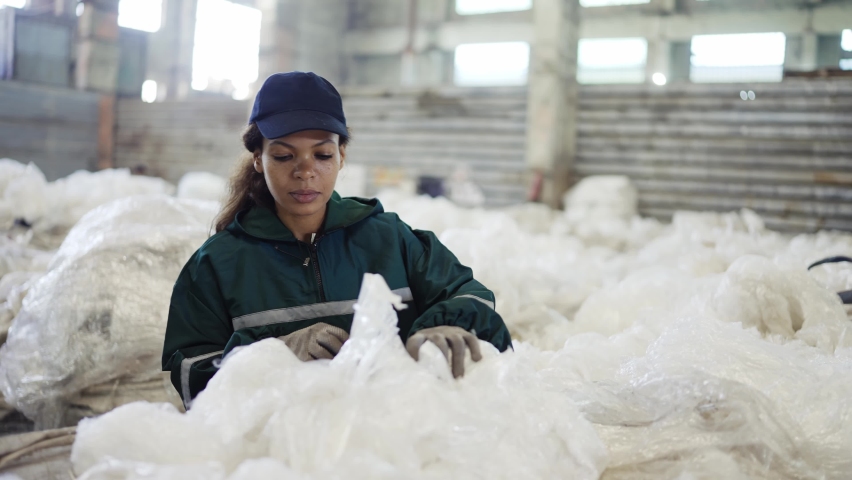 An African-American woman in a special uniform sorts polyethylene at a waste recycling plant. Processing of raw materials, recycling. Pollution control | Shutterstock HD Video #1094539233